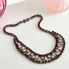 A vintage Astra necklace featuring glowing faux opal cabochons and deep amethyst stones in a double‑row midcentury design, shown on a neutral background to highlight its color and detail.