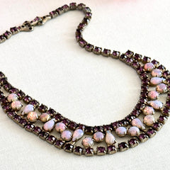 A vintage Astra necklace featuring glowing faux opal cabochons and deep amethyst stones in a double‑row midcentury design, shown on a neutral background to highlight its color and detail.