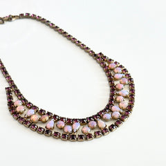 A vintage Astra necklace featuring glowing faux opal cabochons and deep amethyst stones in a double‑row midcentury design, shown on a neutral background to highlight its color and detail.