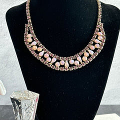 A vintage Astra necklace featuring glowing faux opal cabochons and deep amethyst stones in a double‑row midcentury design, shown on a neutral background to highlight its color and detail.