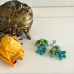 Vintage Austrian blue and green granulated enamel floral clip‑on earrings with rhinestone accents, shown from multiple angles to display their mid‑century design.