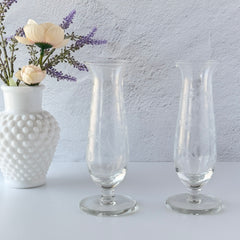 Pair of vintage Avon etched glass pedestal vases with frosted floral design and flared rim.