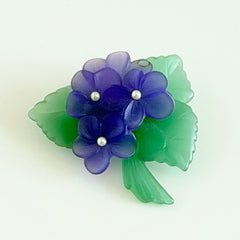 Vintage 1983 Avon brooch with frosted purple resin violets, green leaves, and faux‑pearl centers.