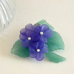 Vintage 1983 Avon brooch with frosted purple resin violets, green leaves, and faux‑pearl centers.