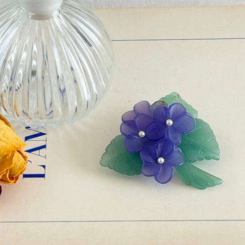 Vintage 1983 Avon brooch with frosted purple resin violets, green leaves, and faux‑pearl centers.
