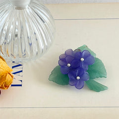 Vintage 1983 Avon brooch with frosted purple resin violets, green leaves, and faux‑pearl centers.