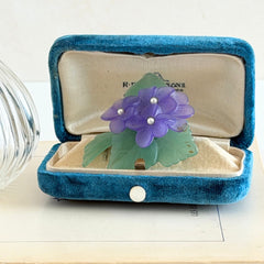 Vintage 1983 Avon brooch with frosted purple resin violets, green leaves, and faux‑pearl centers.