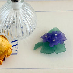 Vintage 1983 Avon brooch with frosted purple resin violets, green leaves, and faux‑pearl centers.