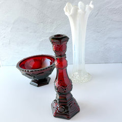 Vintage Avon 1876 Cape Cod Collection ruby red glass perfume bottle and candlestick holder with hexagonal base and ornate embossed pattern, shown with matching bowl and white vase.