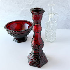 Vintage Avon 1876 Cape Cod Collection ruby red glass perfume bottle and candlestick holder with hexagonal base and ornate embossed pattern, shown with matching bowl and clear decanter.