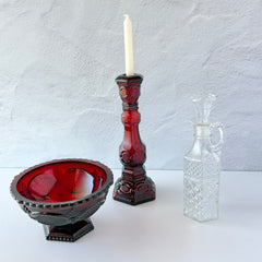 Vintage Avon 1876 Cape Cod Collection ruby red glass perfume bottle and candlestick holder with hexagonal base and ornate embossed pattern, shown with matching bowl and clear decanter.