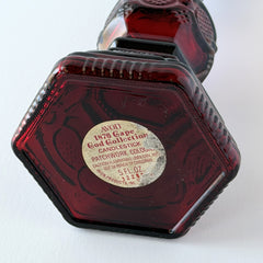 Vintage Avon 1876 Cape Cod Collection ruby red glass perfume bottle and candlestick holder with hexagonal base and ornate embossed pattern.