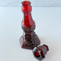 Vintage Avon 1876 Cape Cod Collection ruby red glass perfume bottle and candlestick holder with hexagonal base and ornate embossed pattern.