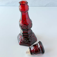 Vintage Avon 1876 Cape Cod Collection ruby red glass perfume bottle and candlestick holder with hexagonal base and ornate embossed pattern.