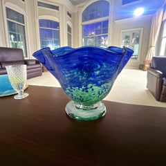 Signed BAGI art glass bowl with a footed base and wavy rim, featuring mottled blue and green swirls. The glass has a glossy finish and sculptural form, with vibrant oceanic and forest tones. Dimensions approximately 5–5½" tall and 7–8" wide.