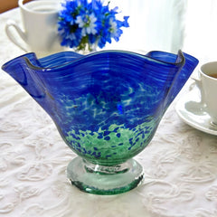 Signed BAGI art glass bowl with a footed base and wavy rim, featuring mottled blue and green swirls. The glass has a glossy finish and sculptural form, with vibrant oceanic and forest tones. Dimensions approximately 5–5½" tall and 7–8" wide.
