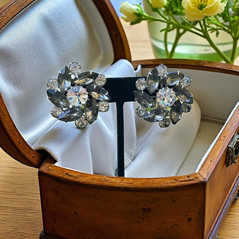 Vintage 1950s silver-tone clip-on earrings with black diamond and clear rhinestones in a radiant pinwheel design; unsigned but crafted with rivet and swedge construction typical of Beau Jewels or Judy Lee, approx. 1¼" diameter, in very good vintage condition with secure clips and brilliant sparkle.