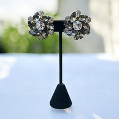 Vintage 1950s silver-tone clip-on earrings with black diamond and clear rhinestones in a radiant pinwheel design; unsigned but crafted with rivet and swedge construction typical of Beau Jewels or Judy Lee, approx. 1¼" diameter, in very good vintage condition with secure clips and brilliant sparkle.