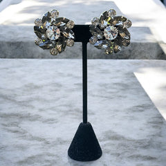 Vintage 1950s silver-tone clip-on earrings with black diamond and clear rhinestones in a radiant pinwheel design; unsigned but crafted with rivet and swedge construction typical of Beau Jewels or Judy Lee, approx. 1¼" diameter, in very good vintage condition with secure clips and brilliant sparkle.