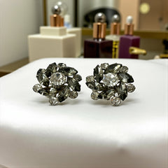 Vintage 1950s silver-tone clip-on earrings with black diamond and clear rhinestones in a radiant pinwheel design; unsigned but crafted with rivet and swedge construction typical of Beau Jewels or Judy Lee, approx. 1¼" diameter, in very good vintage condition with secure clips and brilliant sparkle.