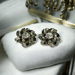 Vintage 1950s silver-tone clip-on earrings with black diamond and clear rhinestones in a radiant pinwheel design; unsigned but crafted with rivet and swedge construction typical of Beau Jewels or Judy Lee, approx. 1¼" diameter, in very good vintage condition with secure clips and brilliant sparkle.
