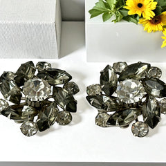 Vintage 1950s silver-tone clip-on earrings with black diamond and clear rhinestones in a radiant pinwheel design; unsigned but crafted with rivet and swedge construction typical of Beau Jewels or Judy Lee, approx. 1¼" diameter, in very good vintage condition with secure clips and brilliant sparkle.