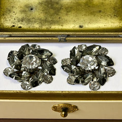 Vintage 1950s silver-tone clip-on earrings with black diamond and clear rhinestones in a radiant pinwheel design; unsigned but crafted with rivet and swedge construction typical of Beau Jewels or Judy Lee, approx. 1¼" diameter, in very good vintage condition with secure clips and brilliant sparkle.