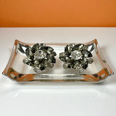 Vintage 1950s silver-tone clip-on earrings with black diamond and clear rhinestones in a radiant pinwheel design; unsigned but crafted with rivet and swedge construction typical of Beau Jewels or Judy Lee, approx. 1¼" diameter, in very good vintage condition with secure clips and brilliant sparkle.