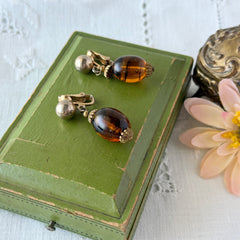Vintage 1950s Bergère clip‑on earrings with oval amber swirl glass beads and gold tone fittings, shown from multiple angles.