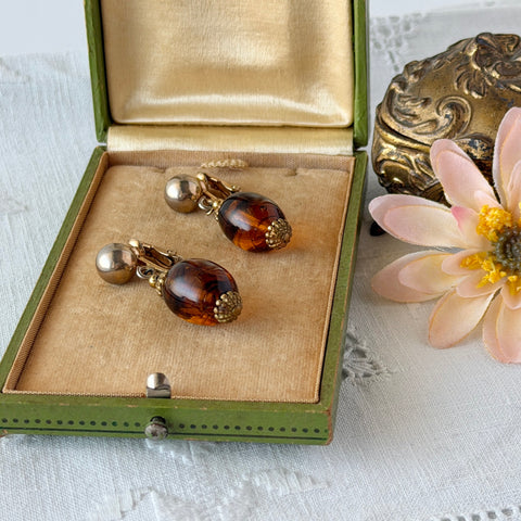 Vintage 1950s Bergère clip‑on earrings with oval amber swirl glass beads and gold tone fittings, shown from multiple angles.