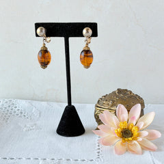 Vintage 1950s Bergère clip‑on earrings with oval amber swirl glass beads and gold tone fittings, shown from multiple angles.