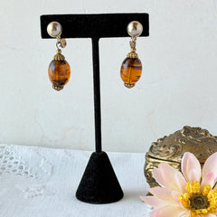 Vintage 1950s Bergère clip‑on earrings with oval amber swirl glass beads and gold tone fittings, shown from multiple angles.
