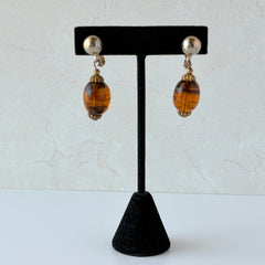 Vintage 1950s Bergère clip‑on earrings with oval amber swirl glass beads and gold tone fittings, shown from multiple angles.
