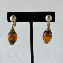 Vintage 1950s Bergère clip‑on earrings with oval amber swirl glass beads and gold tone fittings, shown from multiple angles.