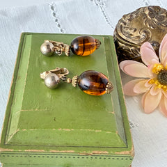 Vintage 1950s Bergère clip‑on earrings with oval amber swirl glass beads and gold tone fittings, shown from multiple angles.