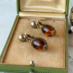 Vintage 1950s Bergère clip‑on earrings with oval amber swirl glass beads and gold tone fittings, shown from multiple angles.