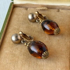 Vintage 1950s Bergère clip‑on earrings with oval amber swirl glass beads and gold tone fittings, shown from multiple angles.