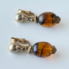 Vintage 1950s Bergère clip‑on earrings with oval amber swirl glass beads and gold tone fittings, shown from multiple angles.