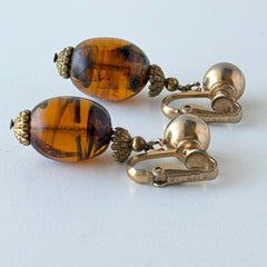 Vintage 1950s Bergère clip‑on earrings with oval amber swirl glass beads and gold tone fittings, shown from multiple angles.