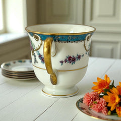 Vintage Black Knight Hohenberg Bavaria porcelain demi-tasse teacup in Monceau pattern; white base with multicolored floral design, teal and gold scrollwork near rim, and gold-trimmed handle and pedestal base.