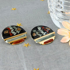 Vintage 1980s black, green, and rust enamel geometric gold‑tone circle post earrings on original Complements card, shown on grey fabric background.