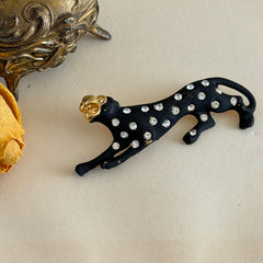 Black matte enamel panther brooch with clear rhinestones and gold tone accents, vintage 1990s animal jewelry.