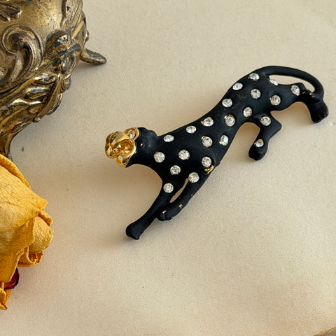 Black matte enamel panther brooch with clear rhinestones and gold tone accents, vintage 1990s animal jewelry.