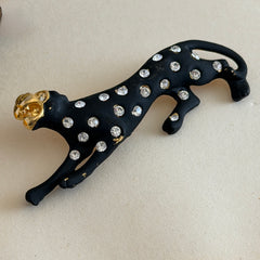 Black matte enamel panther brooch with clear rhinestones and gold tone accents, vintage 1990s animal jewelry.