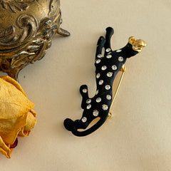 Black matte enamel panther brooch with clear rhinestones and gold tone accents, vintage 1990s animal jewelry.
