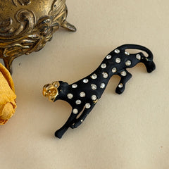Black matte enamel panther brooch with clear rhinestones and gold tone accents, vintage 1990s animal jewelry.