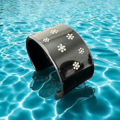A vintage black plastic cuff bracelet featuring a sleek design with clear rhinestones arranged in small floral patterns. The bracelet, likely from the 2000s, is shown in very good condition with minimal surface scratching, adding timeless elegance and eco-conscious charm to any outfit.
