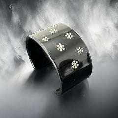 A vintage black plastic cuff bracelet featuring a sleek design with clear rhinestones arranged in small floral patterns. The bracelet, likely from the 2000s, is shown in very good condition with minimal surface scratching, adding timeless elegance and eco-conscious charm to any outfit.