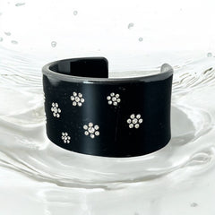 A vintage black plastic cuff bracelet featuring a sleek design with clear rhinestones arranged in small floral patterns. The bracelet, likely from the 2000s, is shown in very good condition with minimal surface scratching, adding timeless elegance and eco-conscious charm to any outfit.