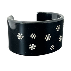 A vintage black plastic cuff bracelet featuring a sleek design with clear rhinestones arranged in small floral patterns. The bracelet, likely from the 2000s, is shown in very good condition with minimal surface scratching, adding timeless elegance and eco-conscious charm to any outfit.